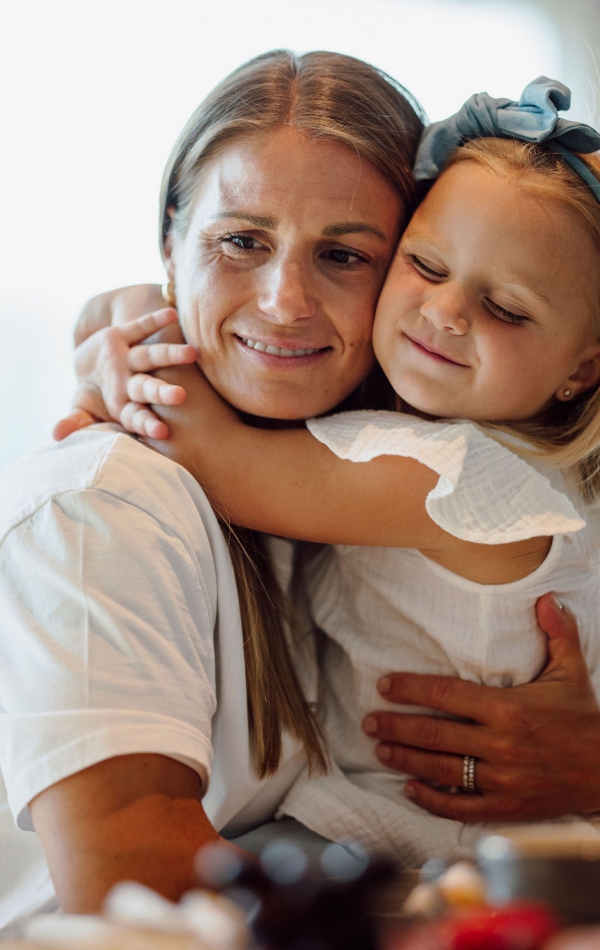 Blondes Mädchen umarmt lächelnde Mutter